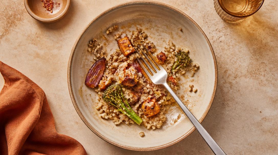A finished meal of grains and roasted vegetables in a ceramic bowl